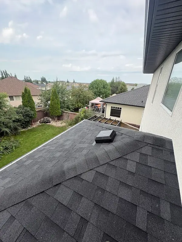 Charcoal shingles on a lower roof above a backyard with a pergola and lawn