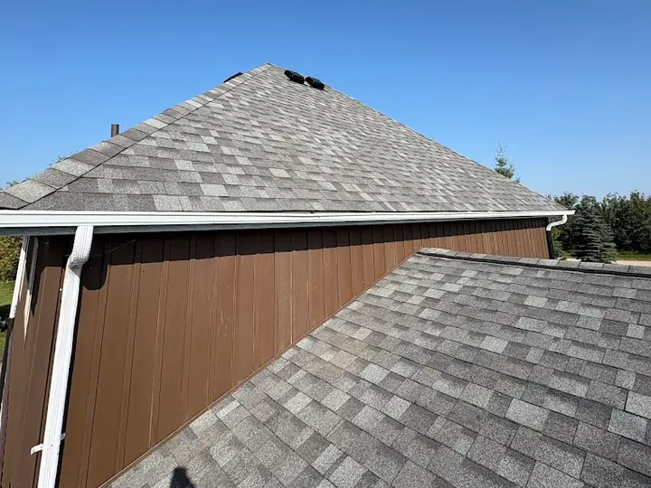 A grey shingle roof with white eavestrough, fascia and a downspout along the edge
