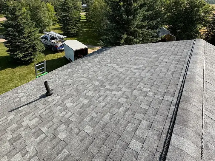 Grey shingles on a new roof with a ridge vent along the peak, and a work truck and trailer in the yard below