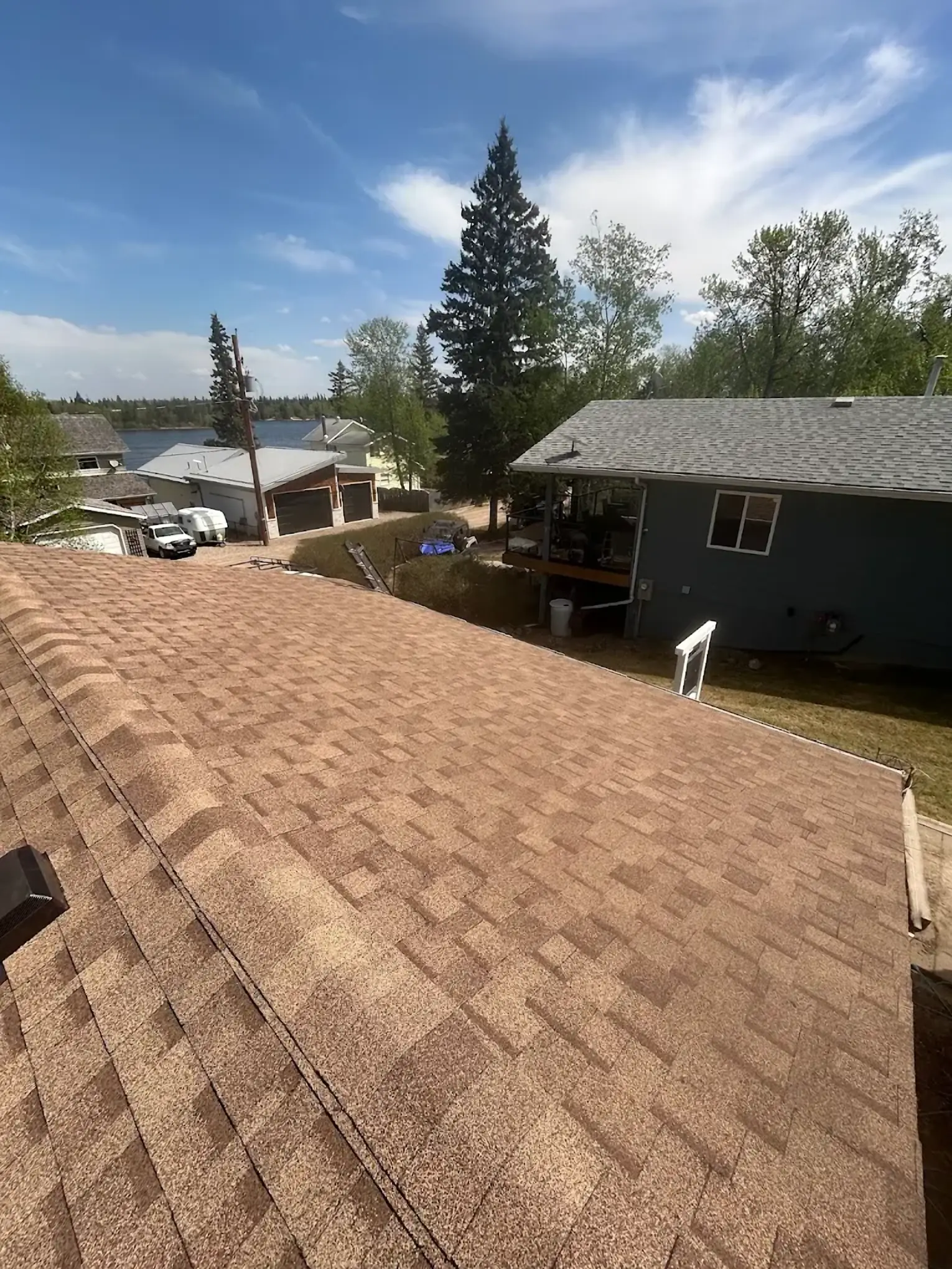 Tan shingles on a new roof looking out over a lake, spruce trees and the neighbouring houses